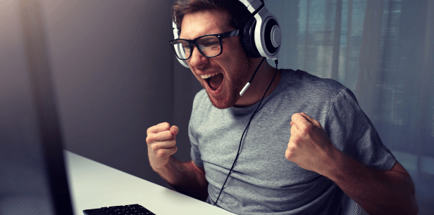 Young man sits in front of his PC and throws his hands up. He is happy about an Epic Moment and experiences the in-game message consciously and positively.