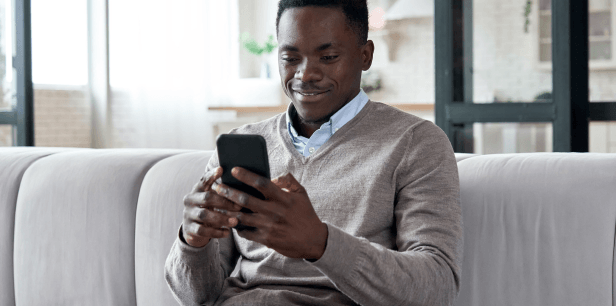 A man sits on a sofa making his donation from the comfort of his smartphone. The image is meant to highlight our easy approach to donating.