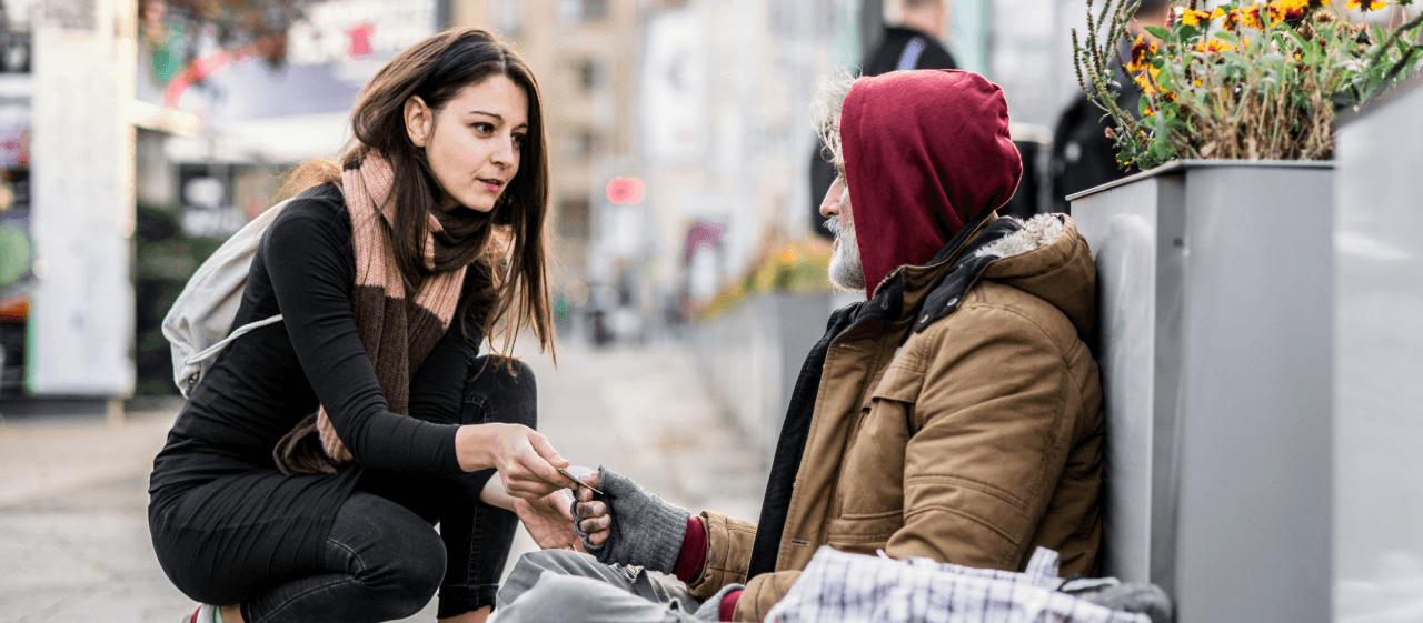 Eine junge Frau hilft einem obdachlosen Mann. Anderen zu helfen ist ein schönes und erfüllendes Gefühl.