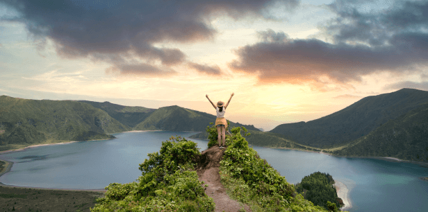 A woman experiences her perfect moment on a summit overlooking a lake.